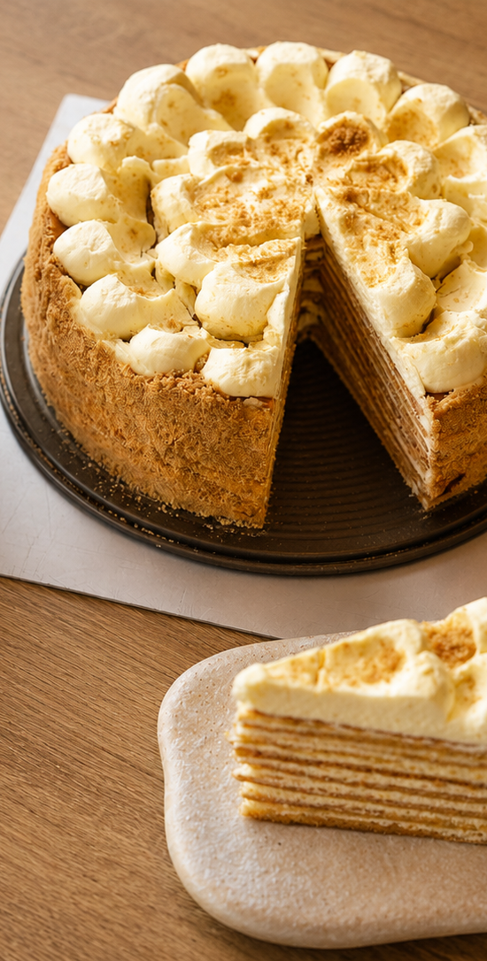 A whole Neeko Bakery honey crepe cake with one slice removed, sitting on a wooden cafe table next to a Neeko branded paper coffee cup.